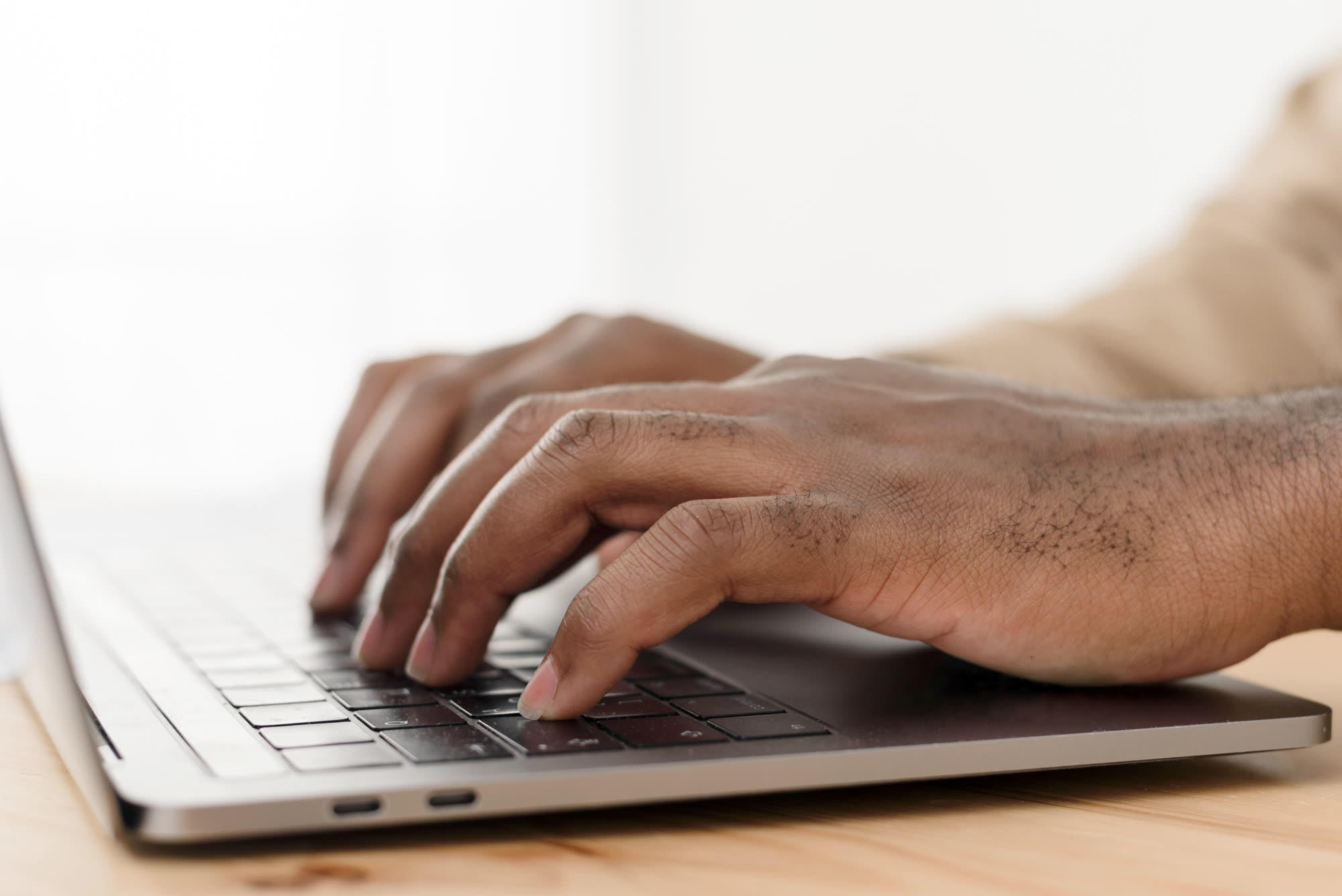 Hands of a Black businessman typing on a laptop while on a phone call