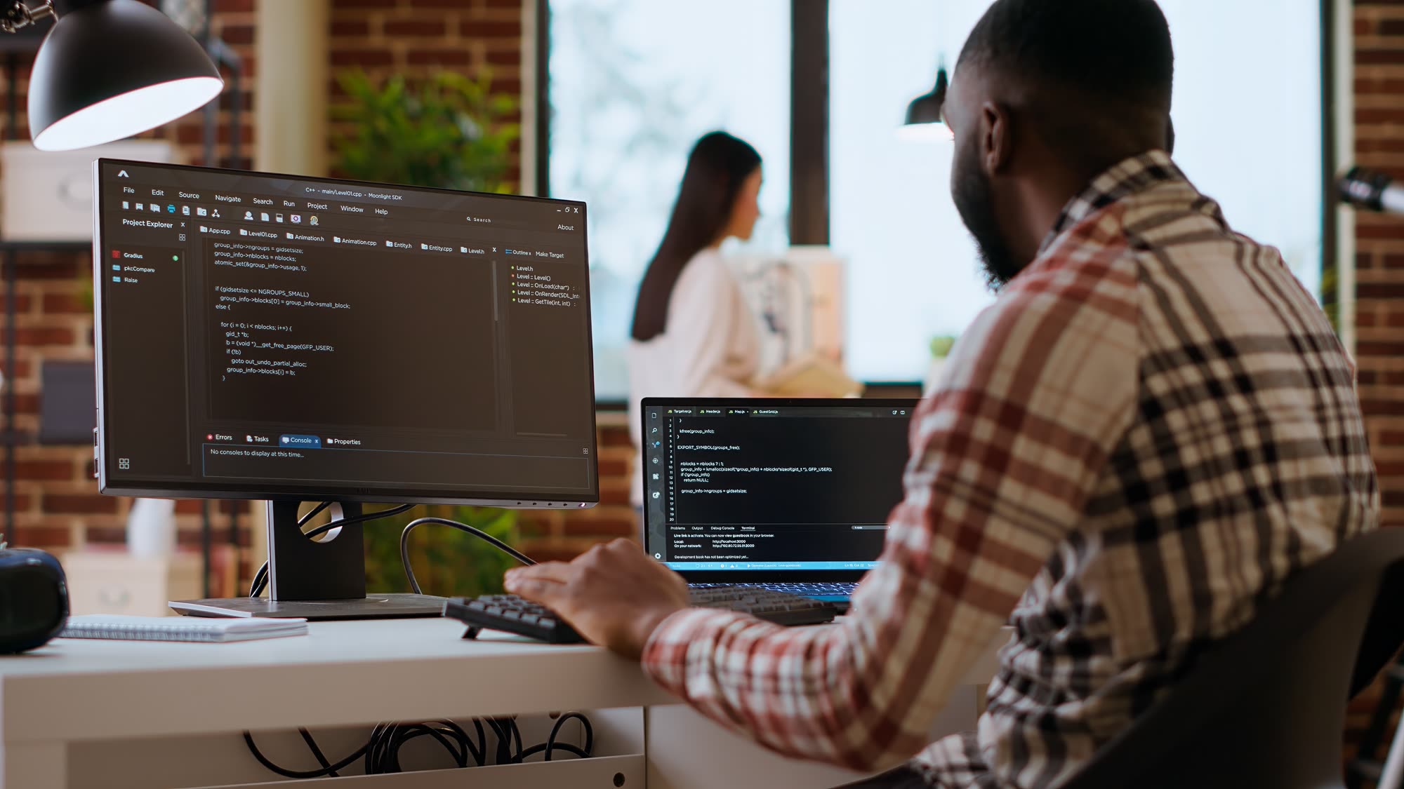 African American IT professional writing code across dual monitors